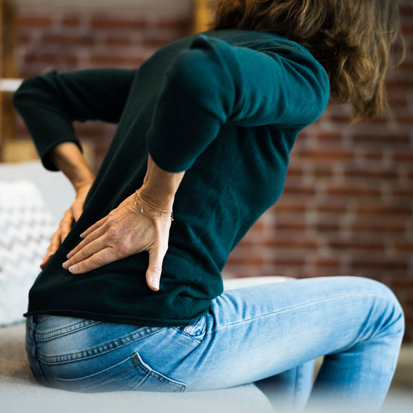 woman sitting on couch with hands on lower back